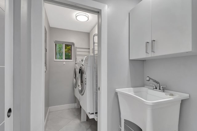 laundry area featuring washing machine and dryer, a sink, light tile patterned floors, baseboards, and cabinet space