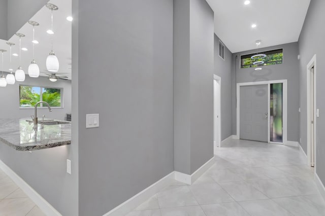 hallway featuring a sink, light tile patterned floors, baseboards, visible vents, and a towering ceiling