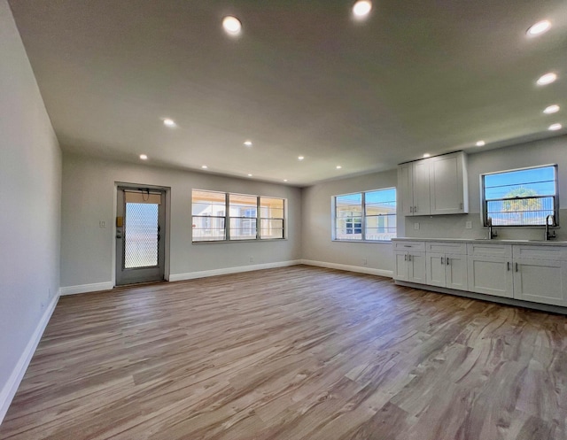 unfurnished living room with a sink, baseboards, light wood-style floors, and recessed lighting