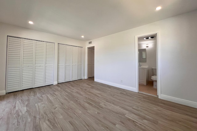 unfurnished bedroom featuring two closets, ensuite bath, wood finished floors, recessed lighting, and baseboards