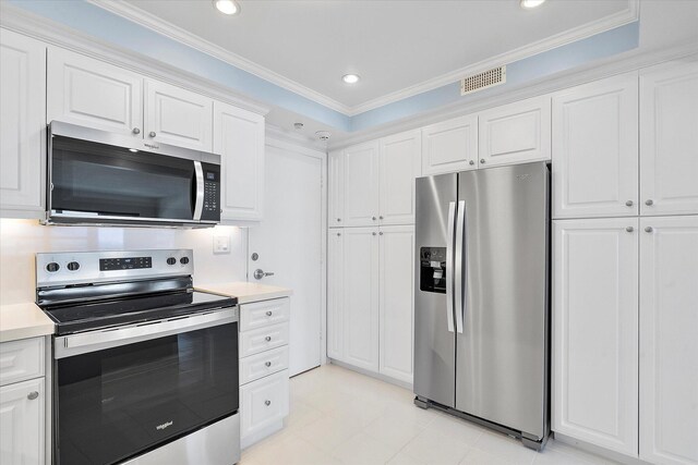kitchen with light countertops, appliances with stainless steel finishes, visible vents, white cabinets, and ornamental molding