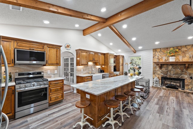 kitchen with light wood-type flooring, a textured ceiling, lofted ceiling with beams, and stainless steel appliances