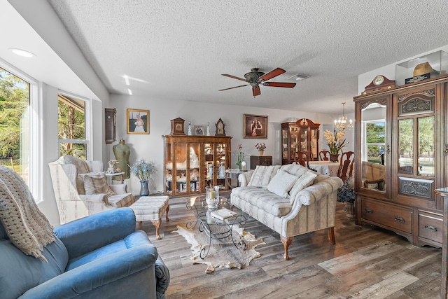 living room featuring visible vents, wood finished floors, a textured ceiling, and ceiling fan with notable chandelier
