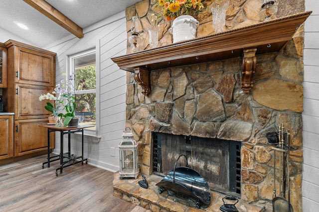 interior details featuring a textured ceiling, baseboards, beamed ceiling, wood finished floors, and a fireplace