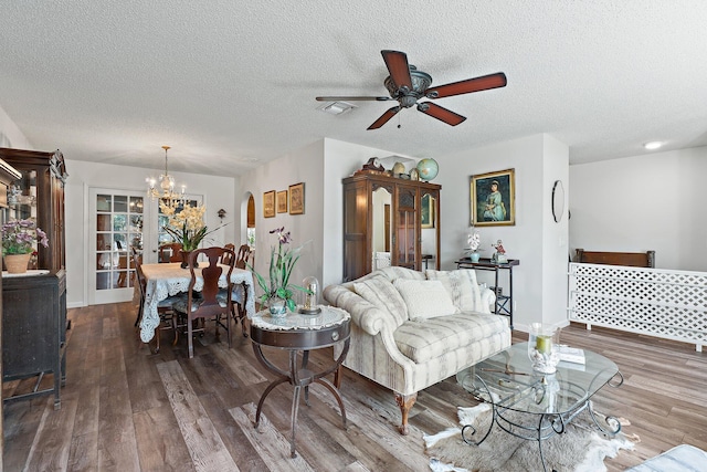 living area featuring a textured ceiling, baseboards, visible vents, ceiling fan with notable chandelier, and wood finished floors
