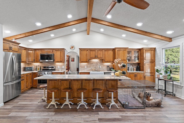 kitchen with lofted ceiling with beams, stainless steel appliances, and brown cabinetry