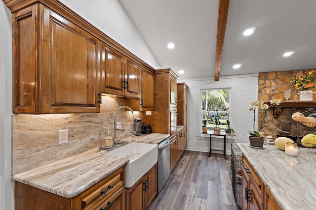 kitchen with brown cabinets, a textured ceiling, stainless steel dishwasher, and dark wood-style floors