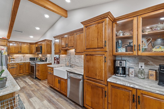 kitchen featuring brown cabinets, visible vents, a sink, lofted ceiling with beams, and appliances with stainless steel finishes