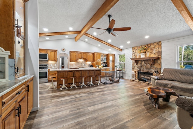 living area with vaulted ceiling with beams, wood finished floors, a textured ceiling, and ceiling fan