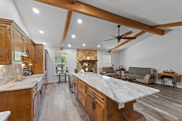 kitchen featuring brown cabinetry, a ceiling fan, vaulted ceiling with beams, and light wood-style flooring