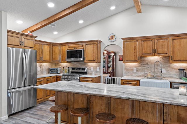 kitchen featuring a sink, lofted ceiling with beams, brown cabinets, a breakfast bar area, and stainless steel appliances
