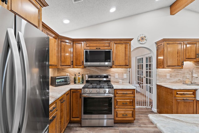 kitchen with vaulted ceiling with beams, brown cabinets, and appliances with stainless steel finishes