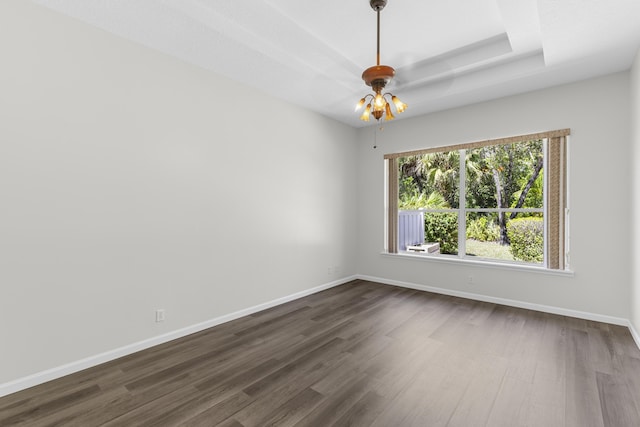 empty room with dark wood finished floors, a tray ceiling, and baseboards