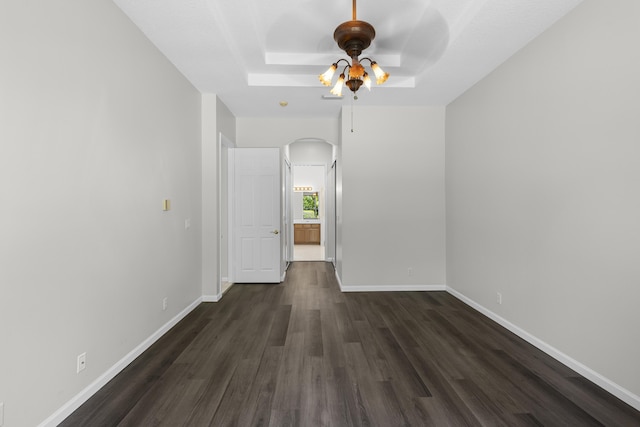 spare room featuring a ceiling fan, a tray ceiling, arched walkways, baseboards, and dark wood-style flooring