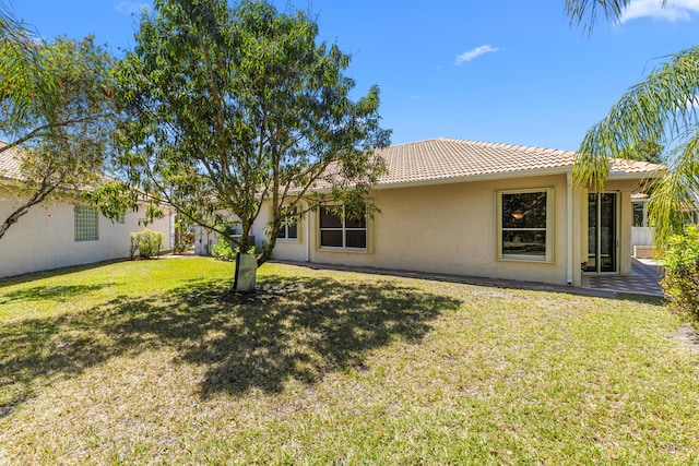 rear view of property with a tiled roof, a yard, and stucco siding
