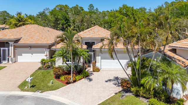 mediterranean / spanish home with decorative driveway, a tiled roof, an attached garage, and stucco siding