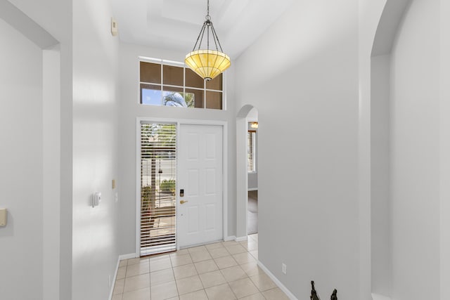 foyer entrance with light tile patterned floors, baseboards, arched walkways, and a towering ceiling