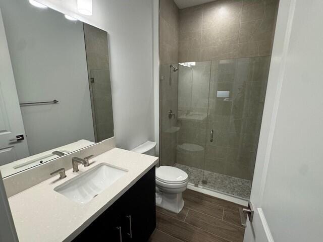 bathroom featuring vanity, toilet, wood finish floors, and a stall shower