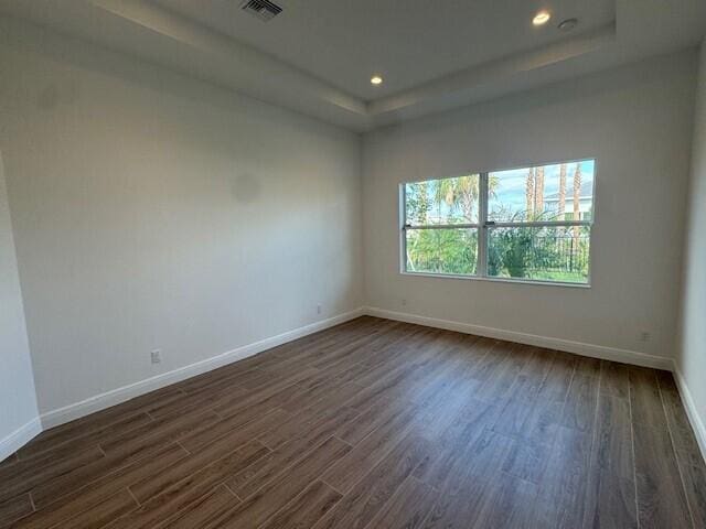 empty room with baseboards, visible vents, dark wood-style floors, and a raised ceiling