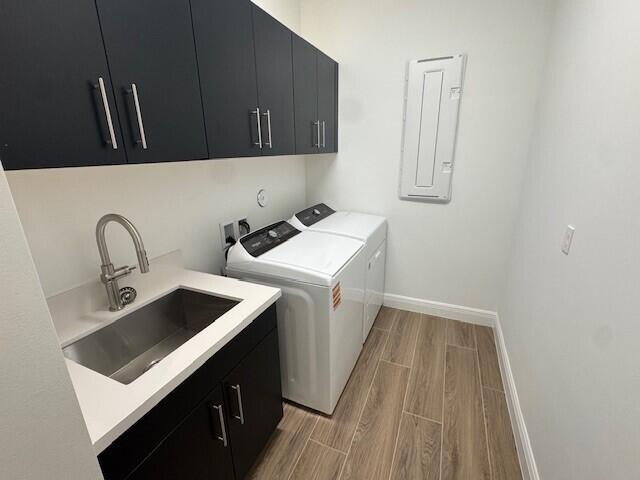 clothes washing area with independent washer and dryer, cabinet space, a sink, wood tiled floor, and electric panel