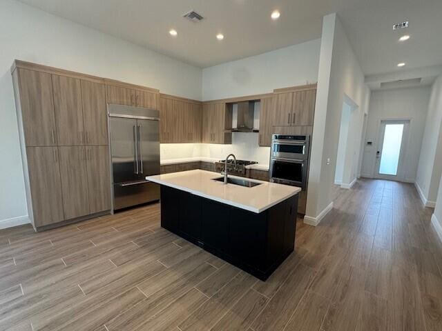 kitchen with light countertops, appliances with stainless steel finishes, wall chimney exhaust hood, and light wood-style floors