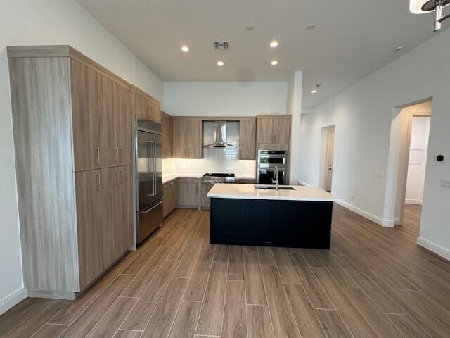 kitchen featuring wall chimney range hood, light countertops, light wood-style floors, and stainless steel appliances
