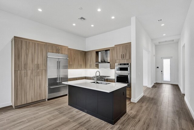 10064 Driftwood Way, Palm Beach Gardens, FL 33412 - kitchen featuring appliances with stainless steel finishes, wall chimney range hood, a sink, light countertops, and light wood-type flooring