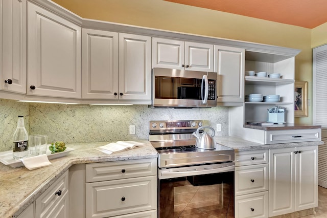 kitchen with backsplash, light stone countertops, white cabinets, stainless steel appliances, and open shelves