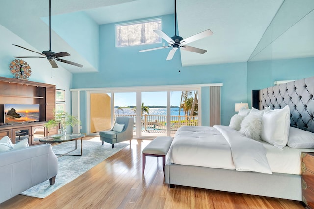 bedroom with a ceiling fan, wood finished floors, a water view, a towering ceiling, and access to outside