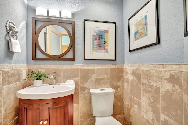 half bathroom with vanity, tile walls, toilet, and a wainscoted wall