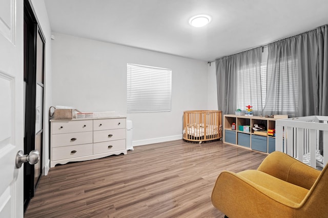 bedroom with baseboards, a crib, and wood finished floors