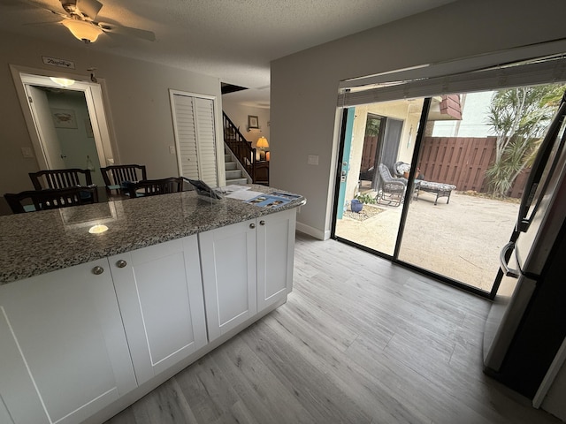 9407 S Ocean Dr Unit 1D, Jensen Beach, FL 34957 - kitchen with light wood-style flooring, fridge, dark stone countertops, white cabinetry, and a textured ceiling