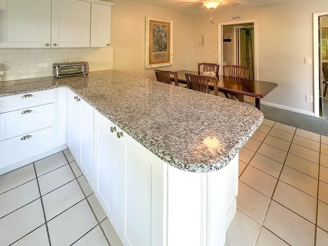 9407 S Ocean Dr Unit 1D, Jensen Beach, FL 34957 - kitchen with a peninsula, light tile patterned floors, decorative backsplash, white cabinetry, and stone counters