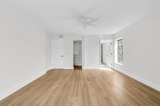 unfurnished bedroom featuring a spacious closet, baseboards, light wood-type flooring, a closet, and a ceiling fan