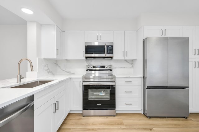 kitchen with a sink, light stone countertops, appliances with stainless steel finishes, and light wood-style flooring