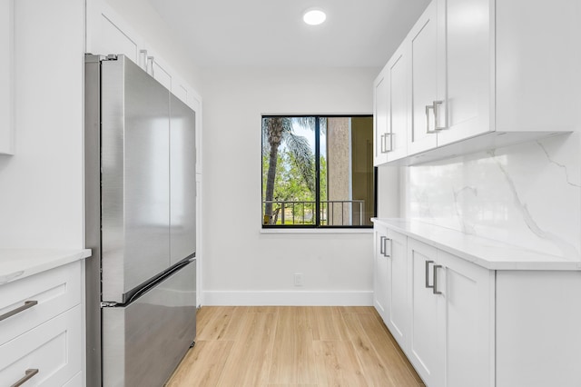 kitchen featuring decorative backsplash, white cabinets, freestanding refrigerator, and light stone countertops