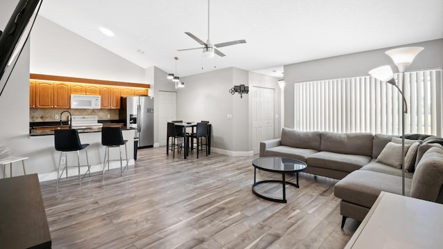 living room featuring a ceiling fan, baseboards, light wood finished floors, and high vaulted ceiling