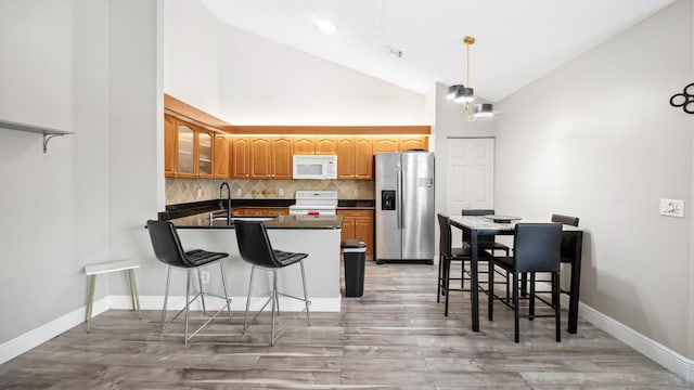 kitchen with white appliances, a peninsula, a sink, glass insert cabinets, and dark countertops