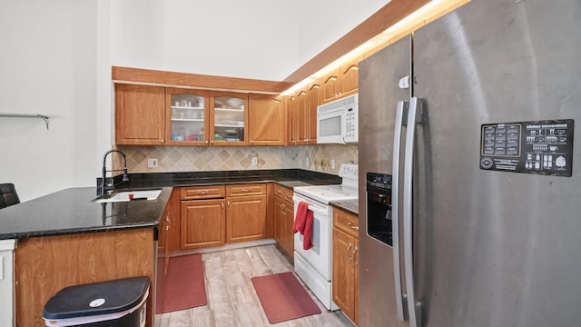 kitchen featuring white appliances, a sink, decorative backsplash, glass insert cabinets, and light wood-style floors