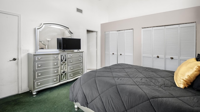 bedroom featuring dark colored carpet, visible vents, and two closets