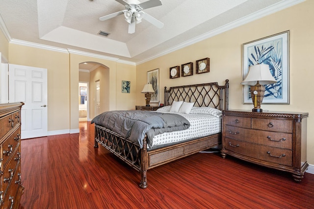 bedroom featuring visible vents, crown molding, arched walkways, a raised ceiling, and dark wood-style flooring