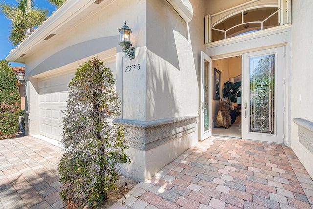 doorway to property with stucco siding, driveway, an AC wall unit, and a garage