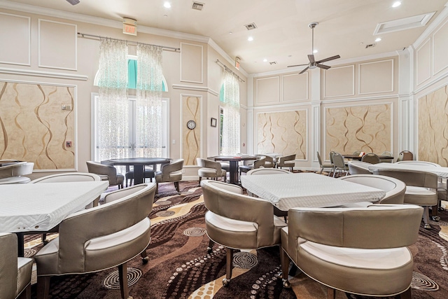 dining area featuring visible vents, ornamental molding, a high ceiling, a decorative wall, and ceiling fan