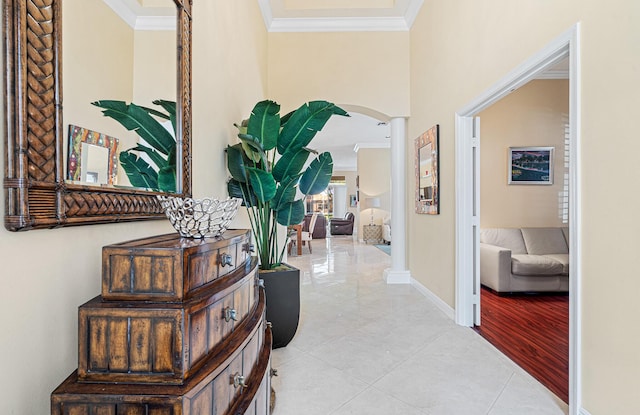 hallway featuring baseboards, ornate columns, light tile patterned flooring, arched walkways, and crown molding