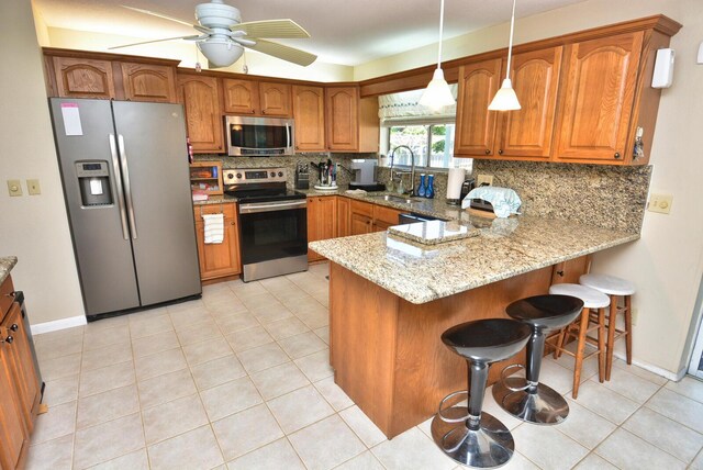 557 SE Seahouse Dr, Port Saint Lucie, FL 34983 - kitchen with a sink, a peninsula, brown cabinetry, stainless steel appliances, and backsplash