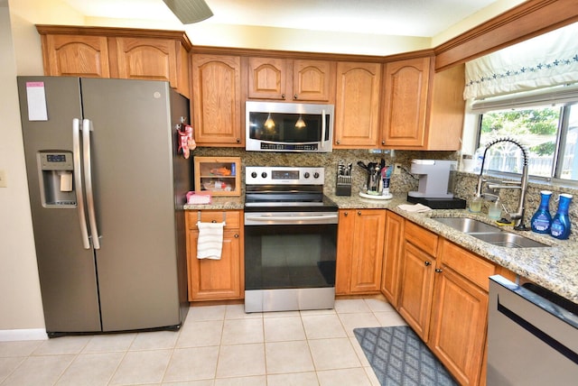 557 SE Seahouse Dr, Port Saint Lucie, FL 34983 - kitchen featuring light stone counters, a sink, stainless steel appliances, brown cabinets, and backsplash