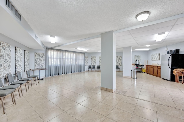 basement with freestanding refrigerator, light tile patterned floors, a paneled ceiling, and visible vents