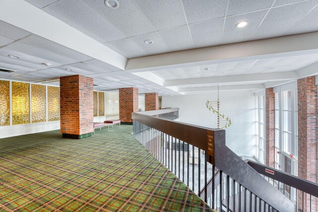 hallway with visible vents, an upstairs landing, carpet flooring, and a drop ceiling