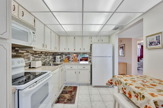 kitchen featuring tasteful backsplash, white appliances, light tile patterned floors, a sink, and a paneled ceiling