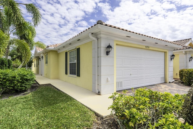 view of side of property with an attached garage, stucco siding, a tiled roof, and driveway